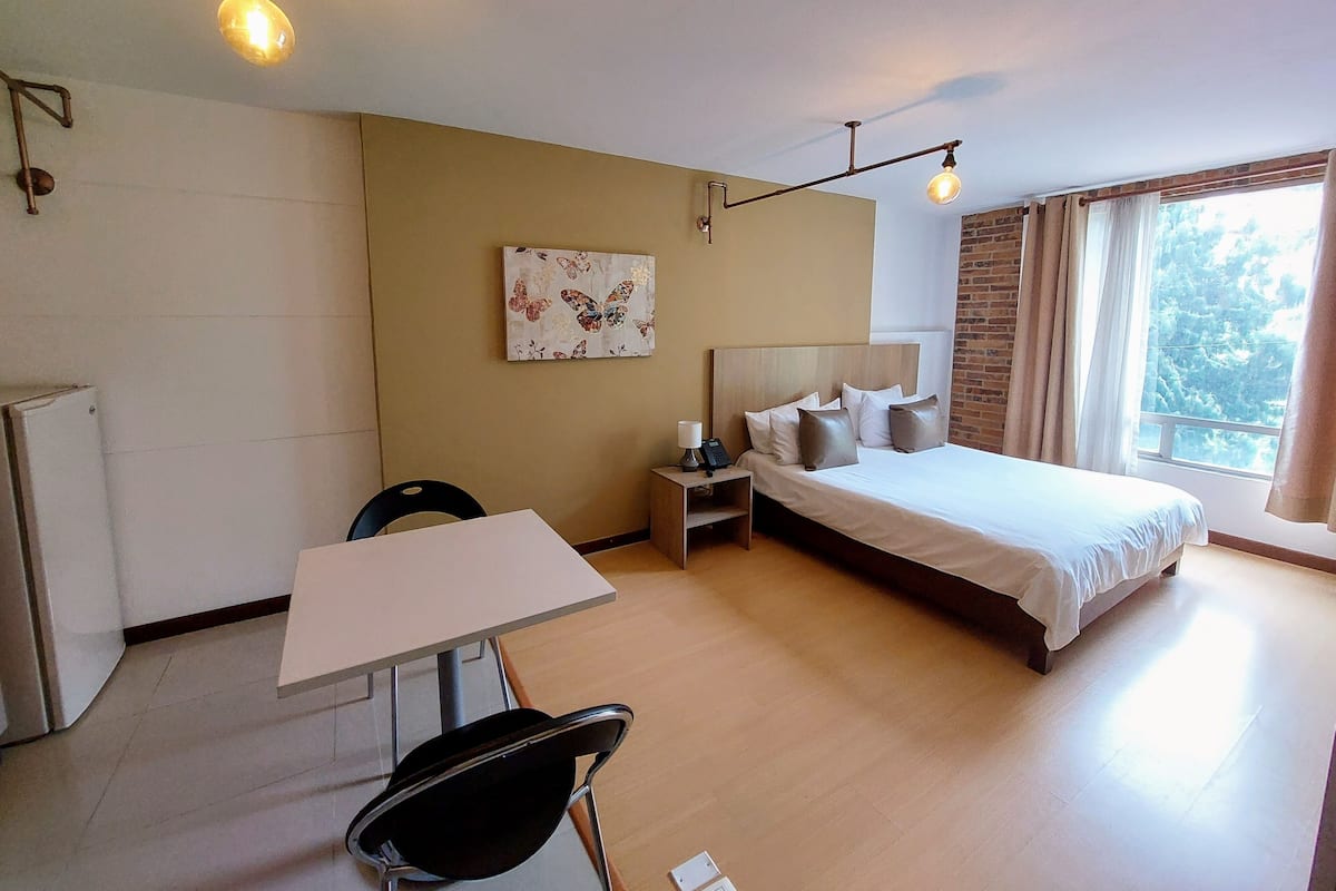 A bedroom with a bed, bedside table, lamp, and a painting on the wall.