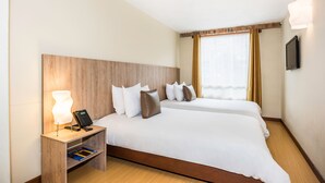 A hotel room with two beds, a bedside table with a lamp, a flat-screen TV, and a window with curtains. - Viaggio Urbano (Bogotá)