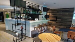 A modern bar area with a marble countertop, black metal shelving, and a variety of bottles. There are wooden tables and chairs arranged for seating. - Viaggio Urbano (Bogotá)