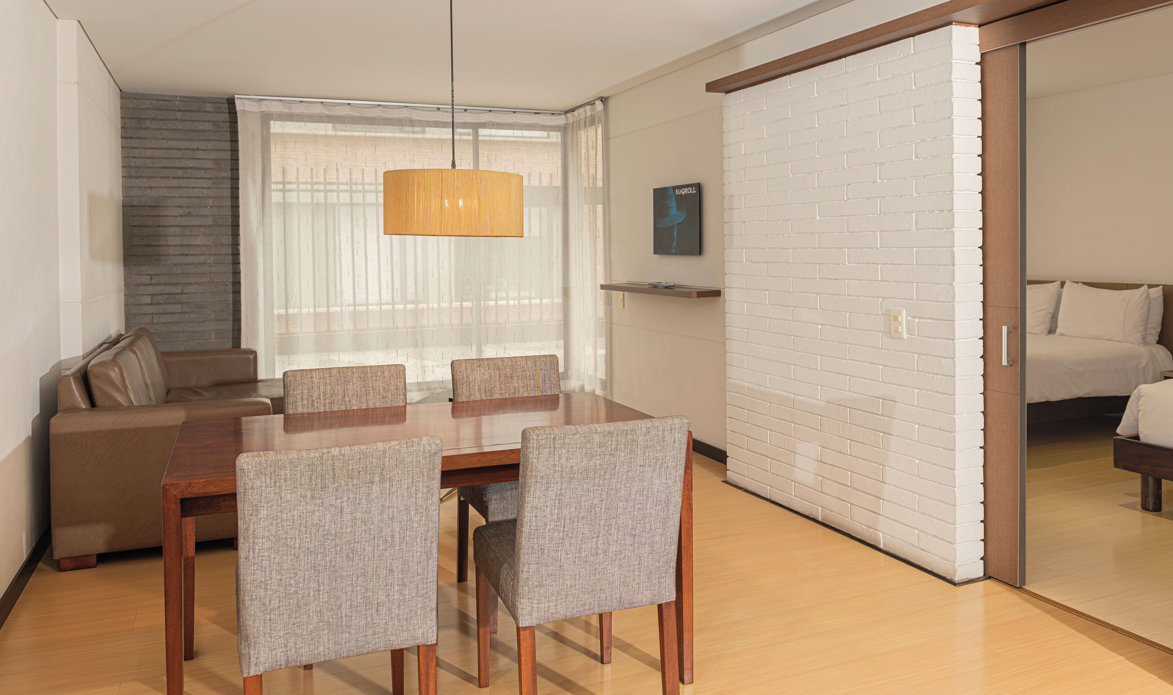 Una habitación de hotel moderna con zona de comedor, sofá, televisor y pared de ladrillo.