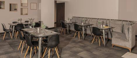A modern dining area with multiple tables and chairs, a sofa, and a door leading to another room.