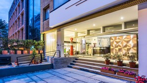 Uma entrada de hotel moderna com fachada de vidro, área de estar externa e plantas em vasos.