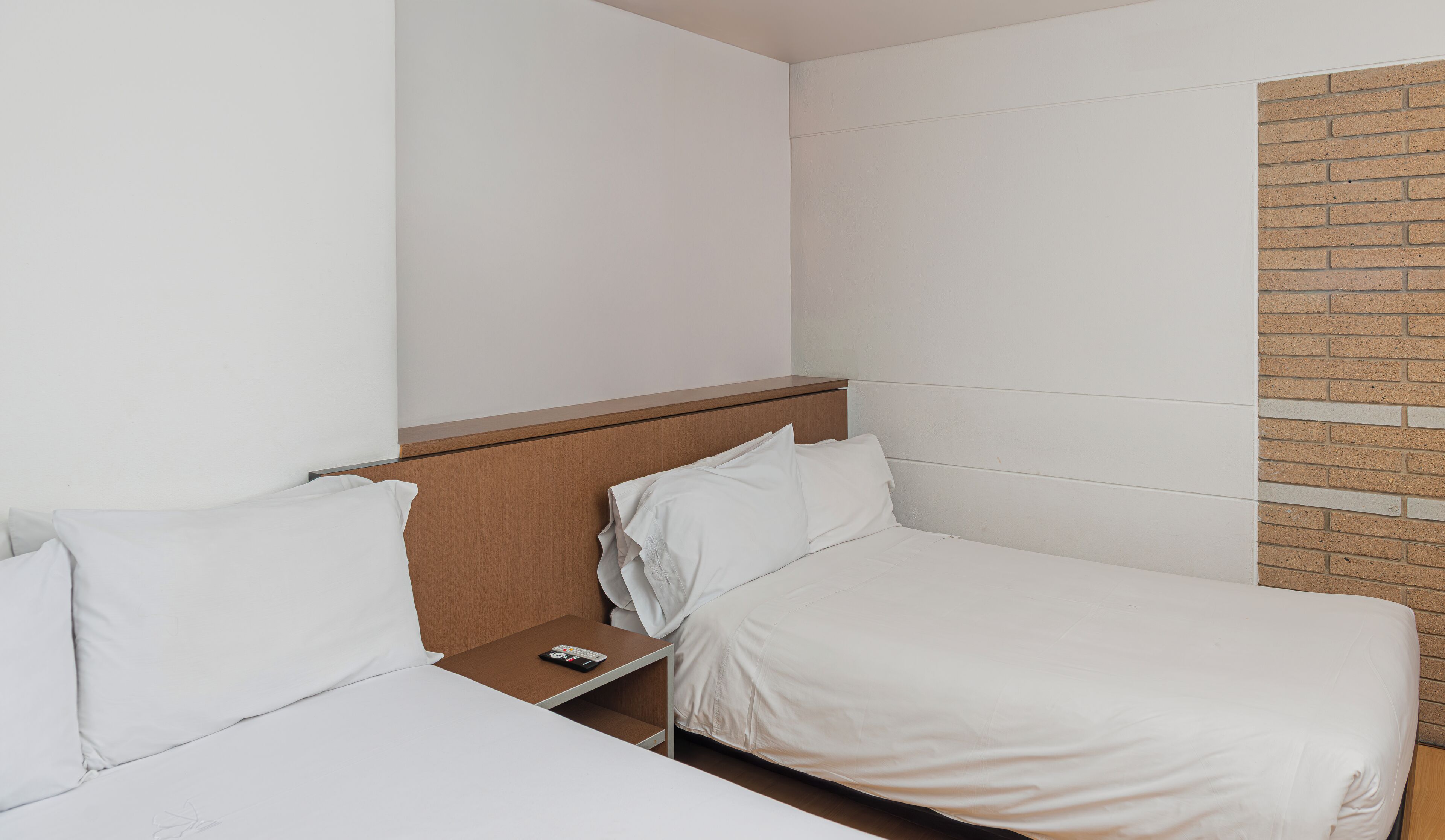 A hotel room with two single beds, a wooden nightstand, and a brick accent wall.