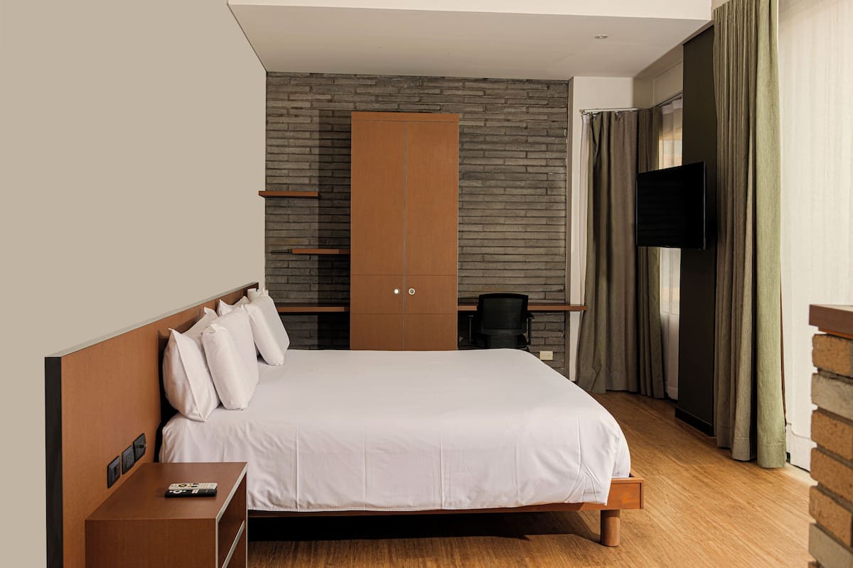 Quarto de hotel moderno com uma cama grande, um guarda-roupa de madeira, uma TV de tela plana e uma parede de destaque em tijolo.