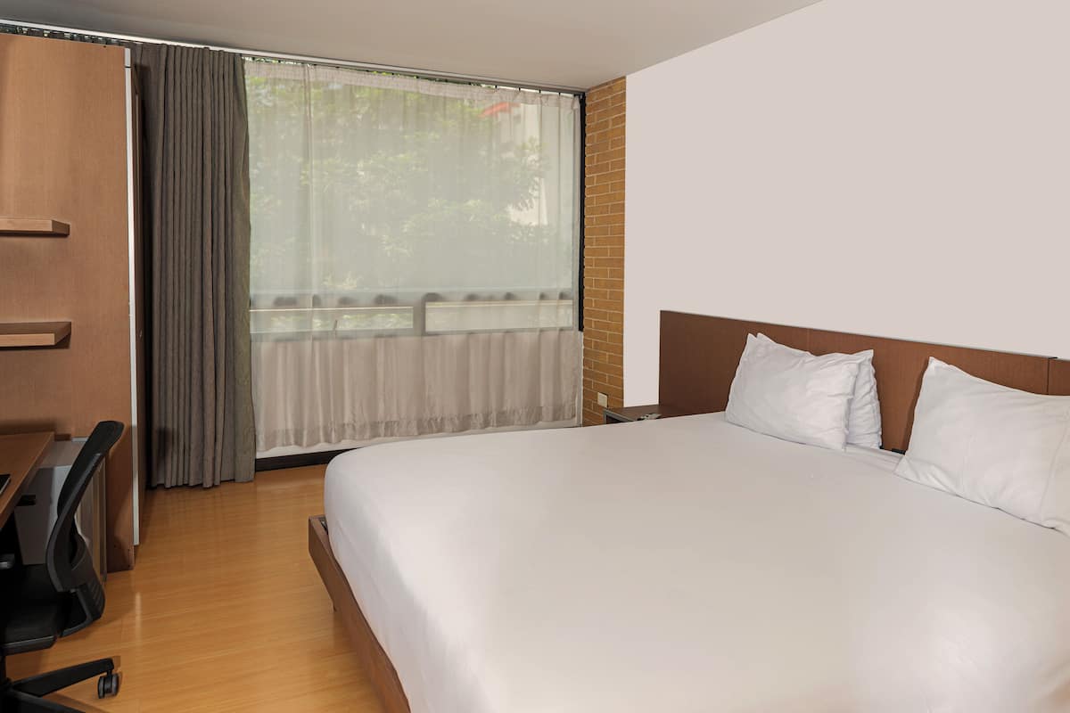 Quarto de hotel com uma cama grande, uma escrivaninha e uma janela com cortinas.