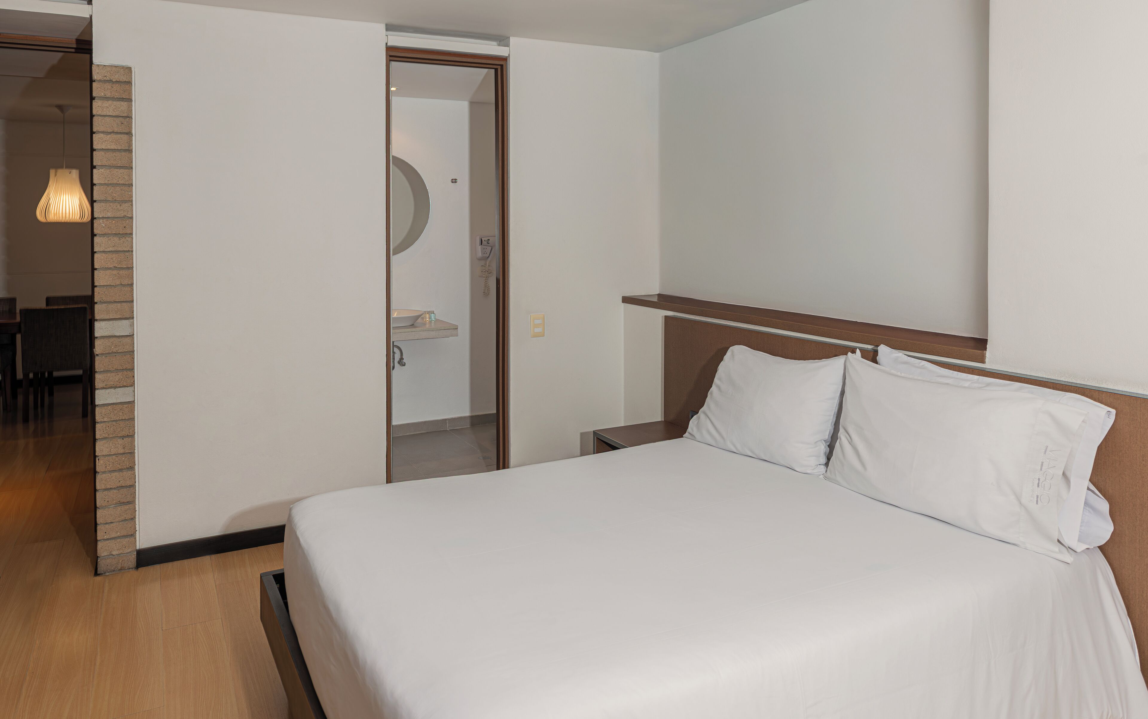 A hotel room with a bed, a wooden headboard, a nightstand, and a bathroom visible through an open door.