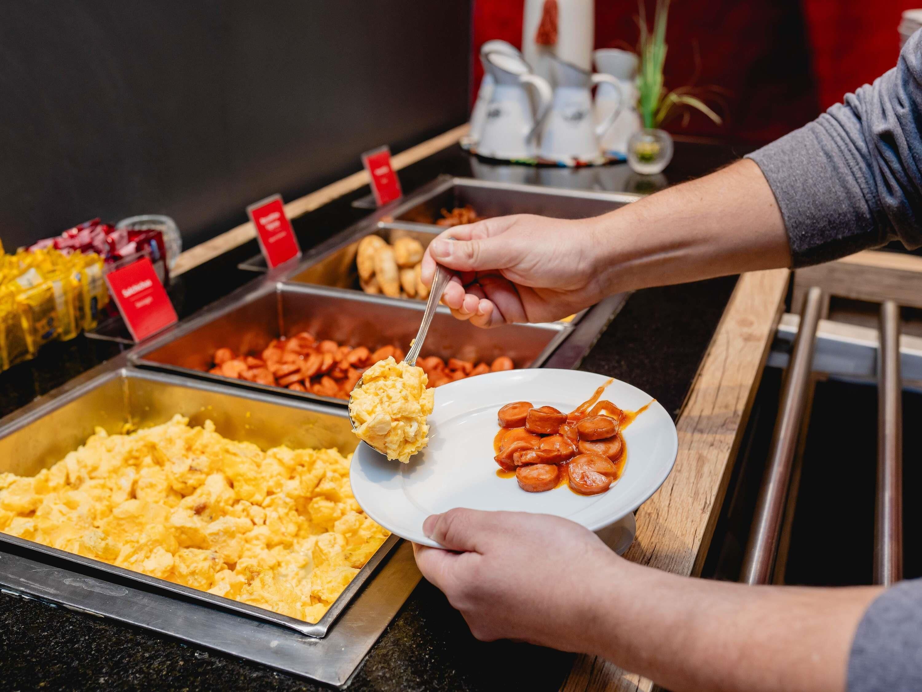 A buffet with various food options, including scrambled eggs and sausages.