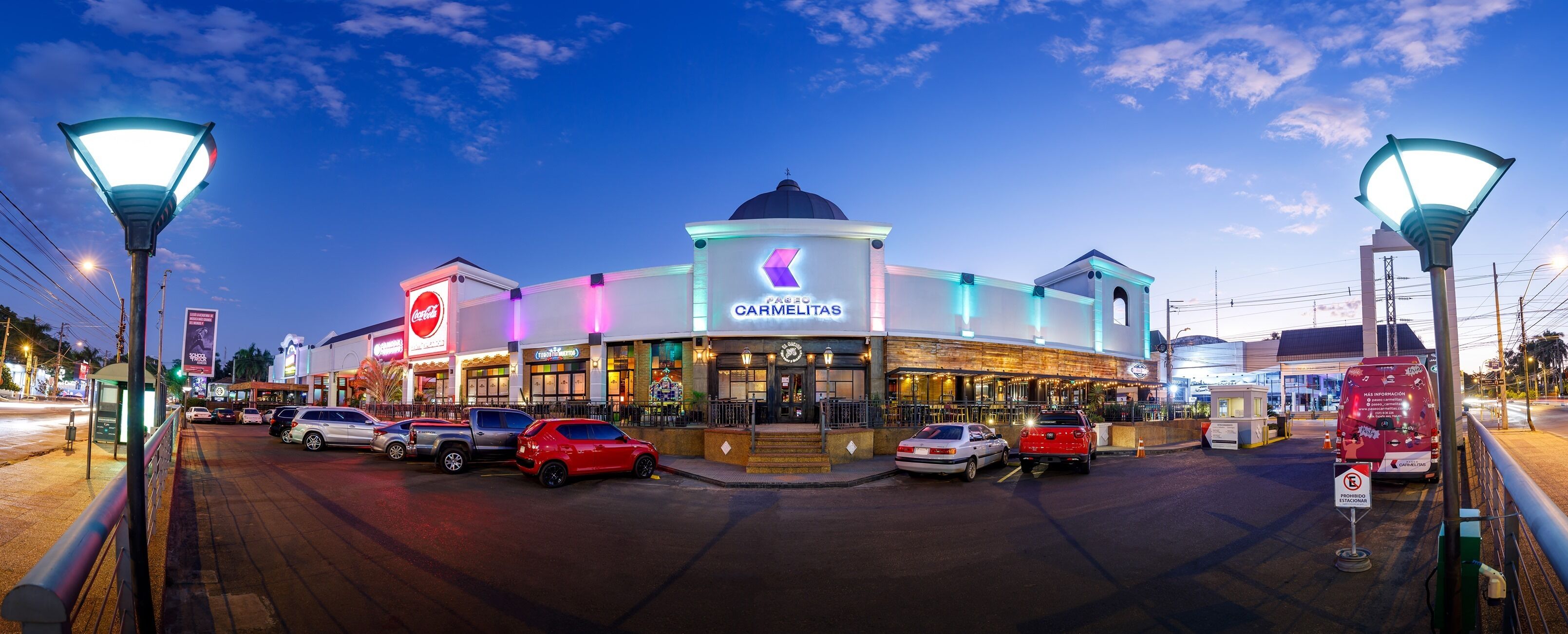 A shopping mall with a prominent 'Carmelitas' store, multiple parking spaces, and a pedestrian walkway.