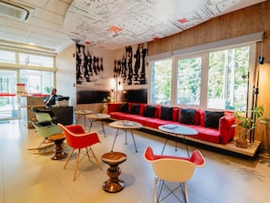 A modern lobby with a red sofa, a reception desk, and a large window offering a view of greenery. - Ibis Asuncion (Asunción)