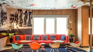 Un espace de détente moderne avec un canapé rouge, des fauteuils colorés et une fresque murale représentant un jeu d’échecs.