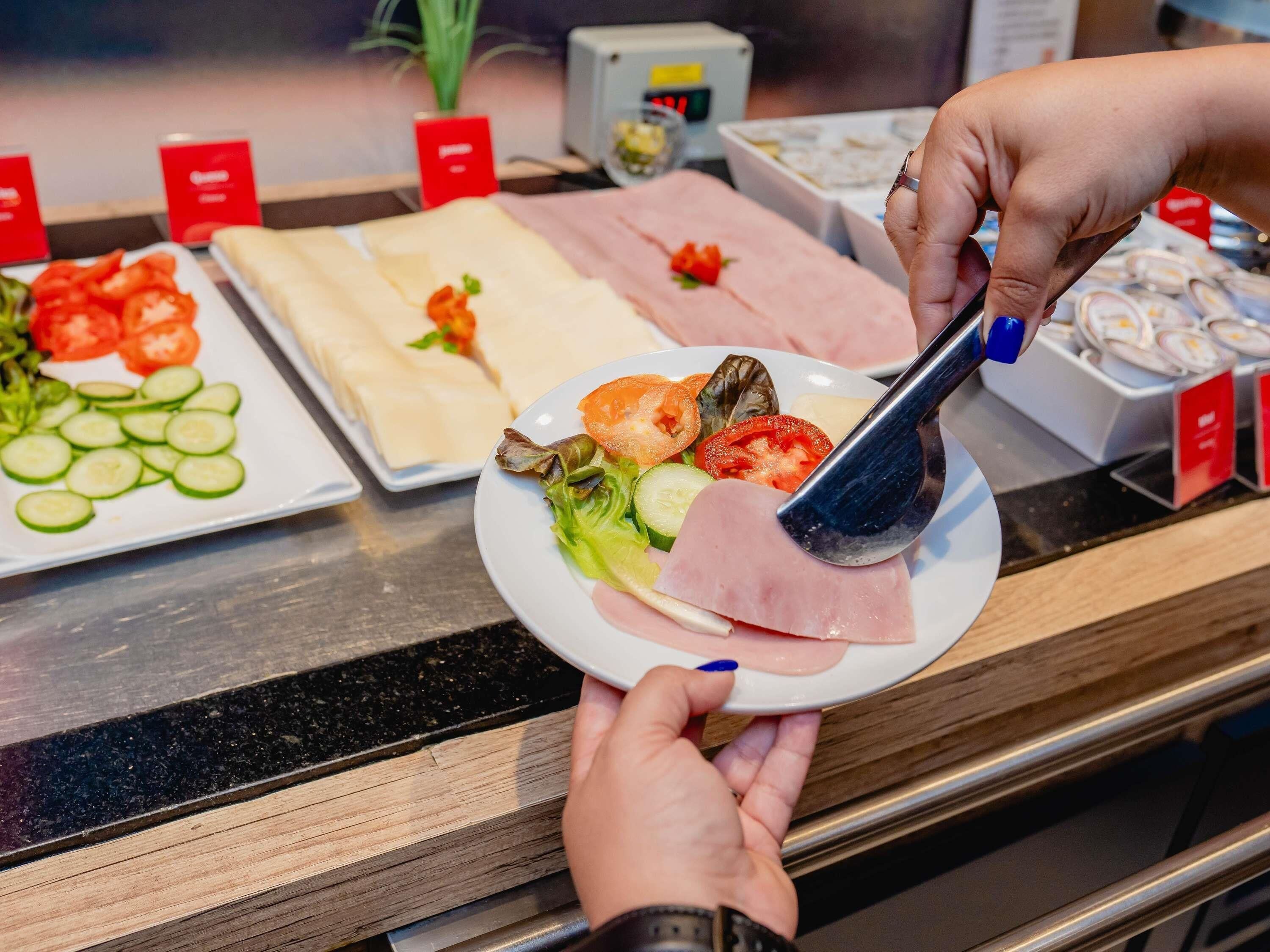 Un bufé con diversos alimentos, incluyendo pepinos en rodajas, tomates, lechuga y diferentes tipos de carne.