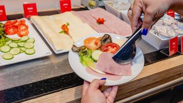 Un bufé con diversos alimentos, incluyendo pepinos en rodajas, tomates, lechuga y diferentes tipos de carne.