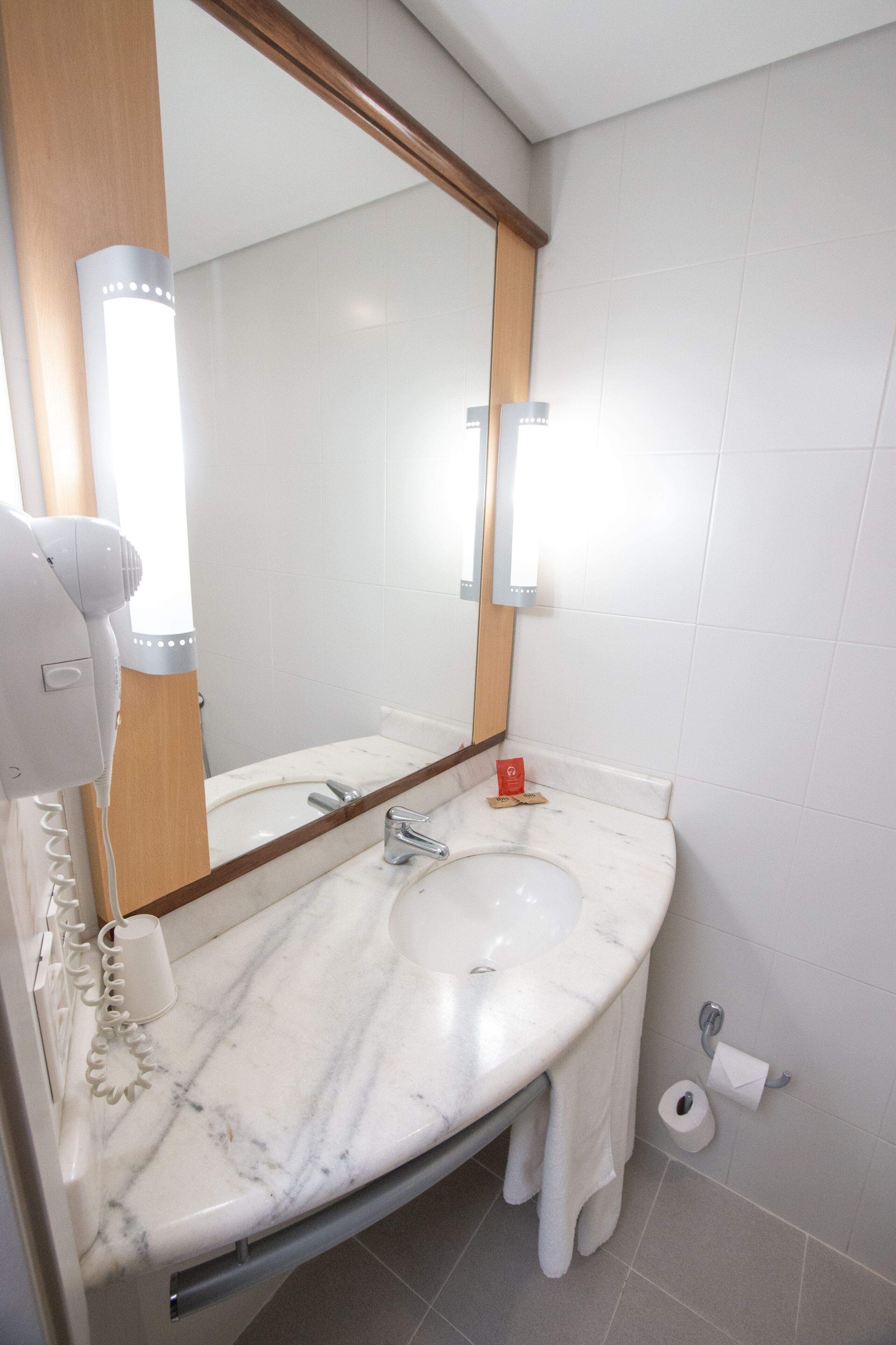 A bathroom with a marble sink, a hairdryer, a mirror, and a toilet paper holder.
