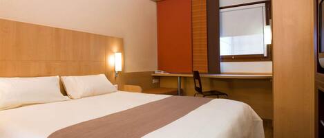 A hotel room with a large bed, a desk, a chair, and a window.