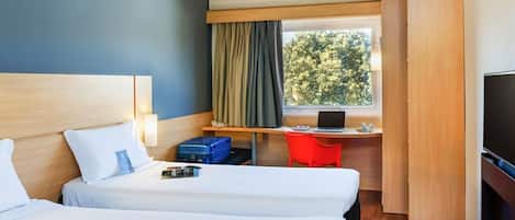 Una habitación de hotel con dos camas, un escritorio con una computadora portátil, un televisor y un ventanal con cortinas.