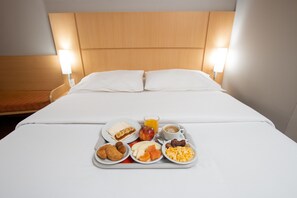 A neatly made bed with white linens, a tray with breakfast items including pastries, fruit, and eggs, and a cup of coffee. - Ibis Asuncion (Asunción)