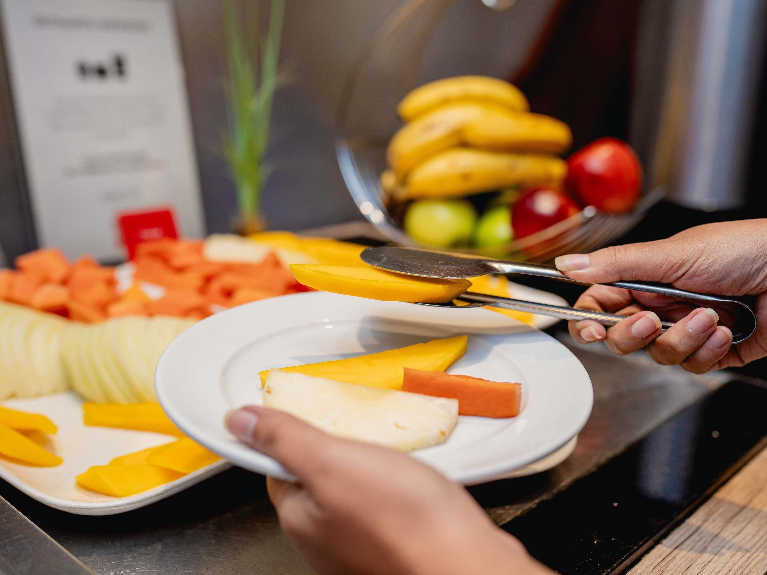 A person cutting fruit with a knife on a plate.