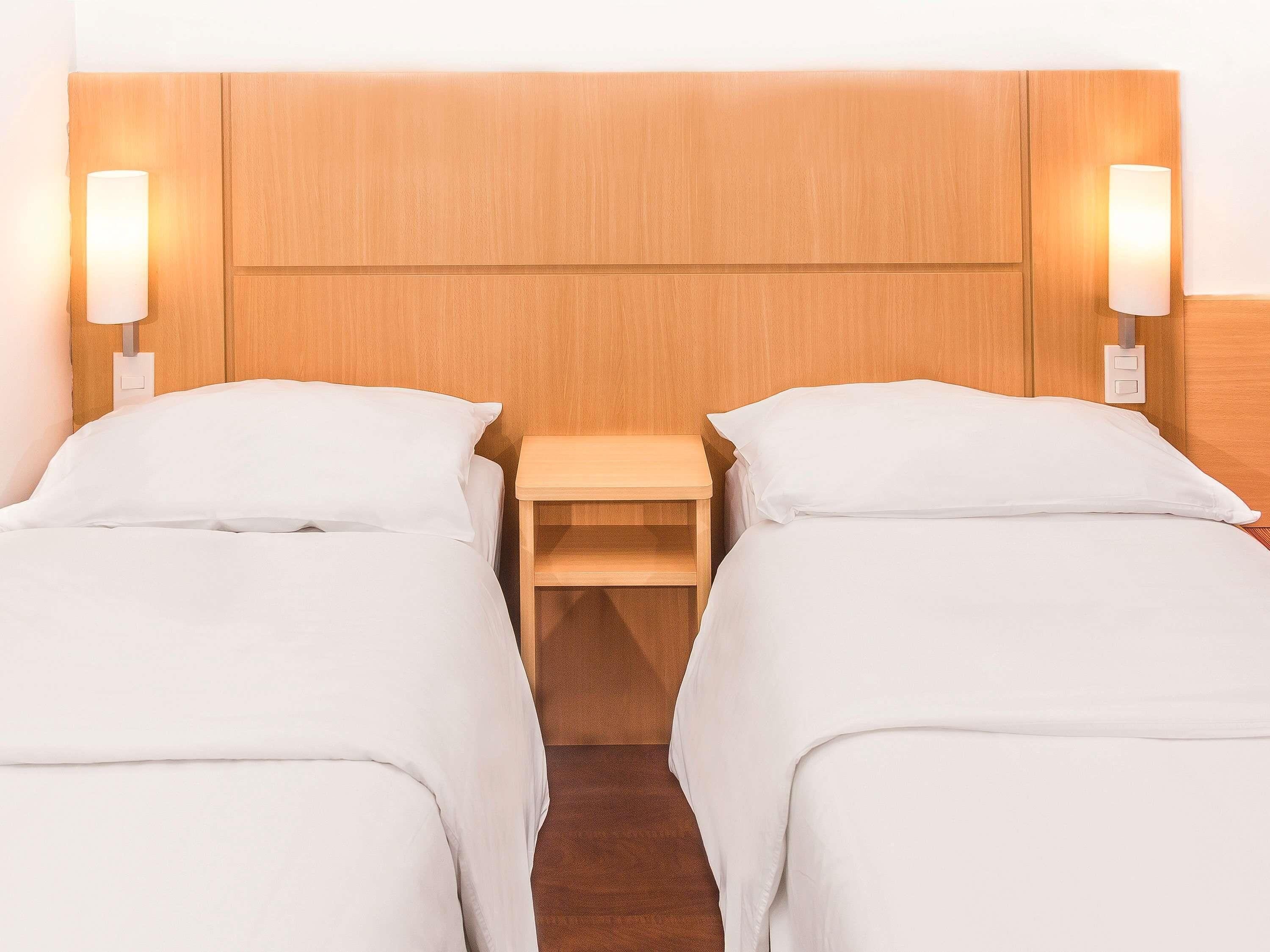 Una habitación de hotel con dos camas individuales, un cabecero de madera, lámparas de noche y una mesita de noche.