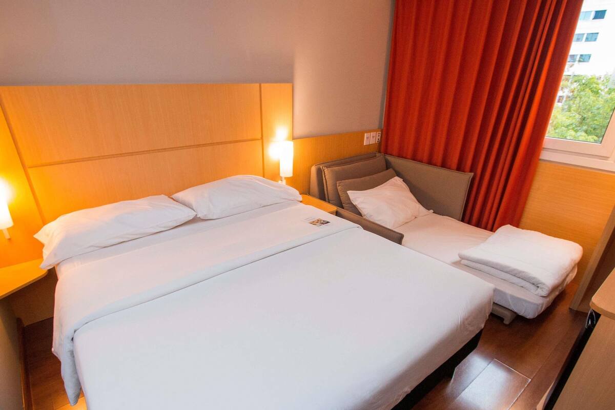 Una habitación de hotel con una cama grande, un sofá, una mesita de noche y una ventana con cortinas.