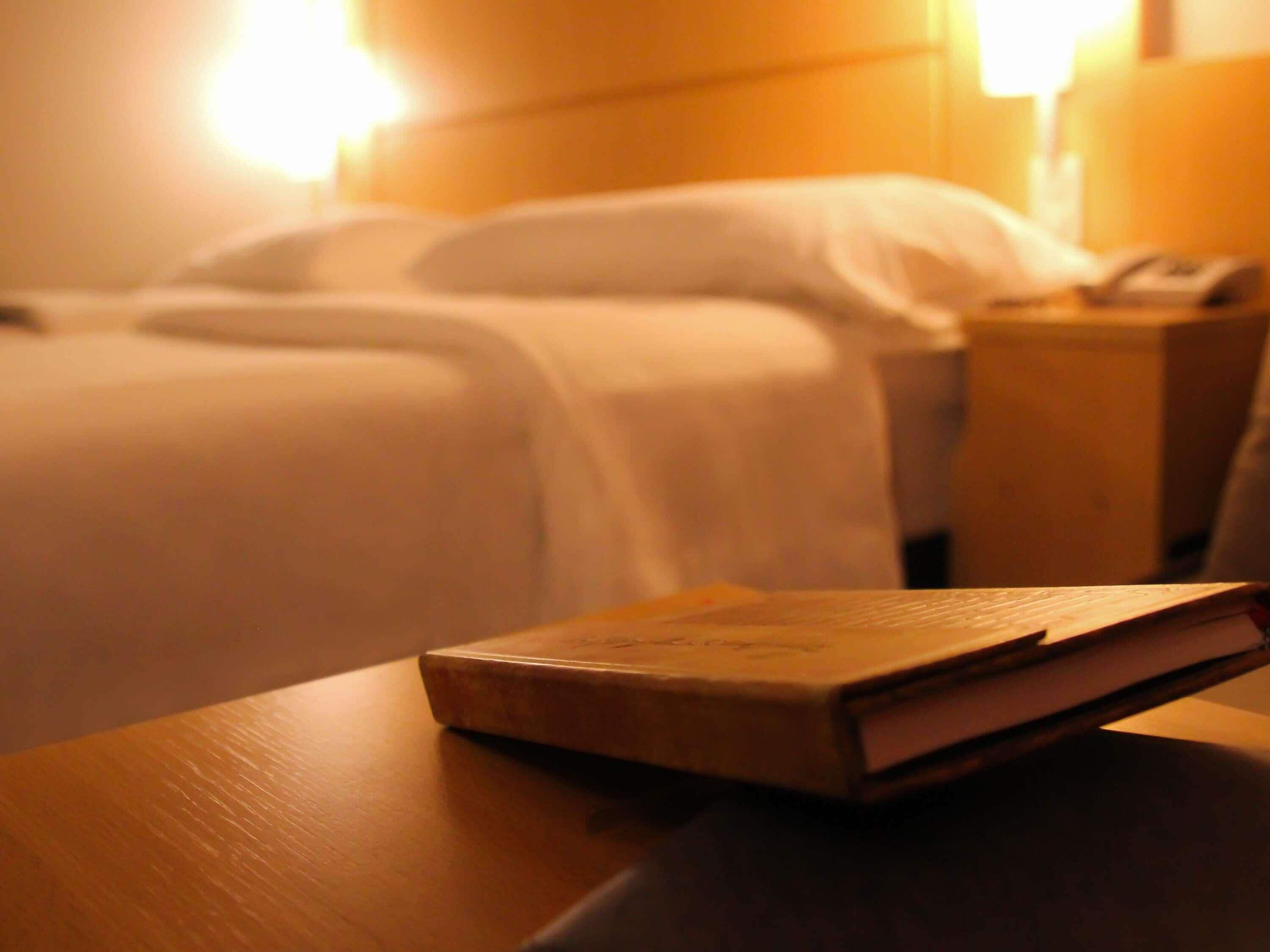 A hotel room with a neatly made bed, a bedside table with a book, and a nightstand with a phone.