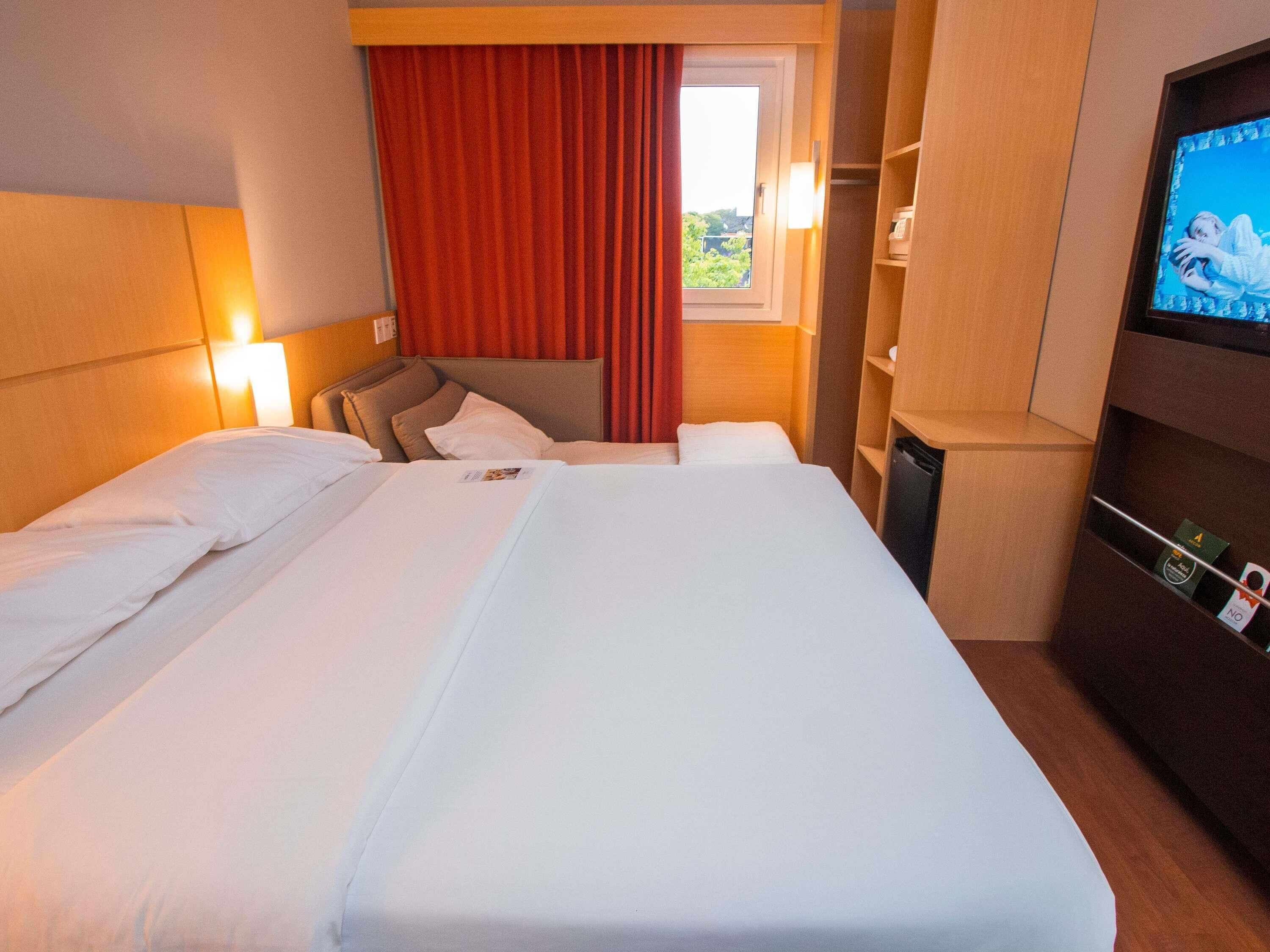 Una camera d'albergo con un letto grande, una televisione, una scrivania e una finestra con tende.