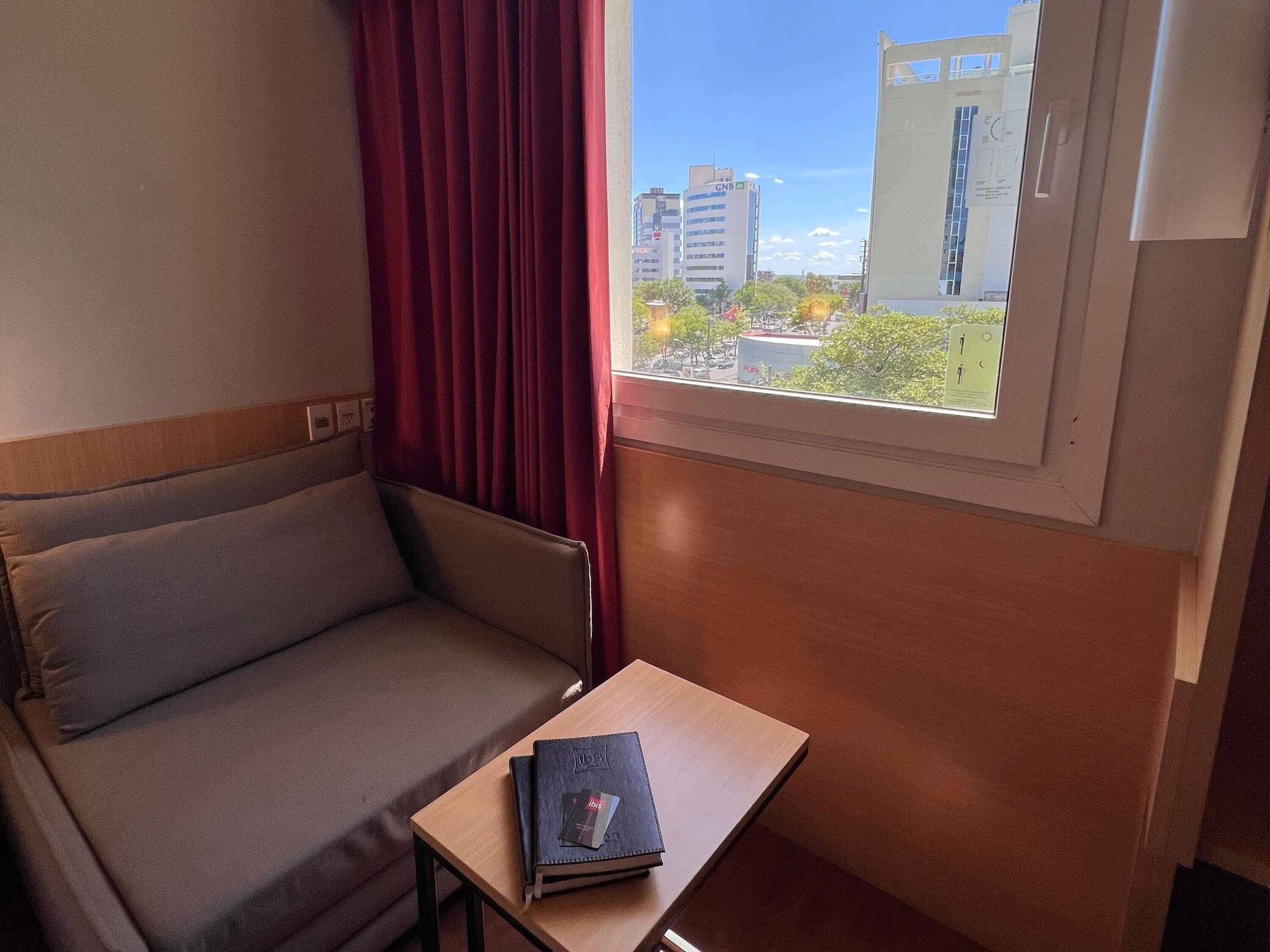 A room with a sofa, a small table, a window with a view of buildings, and a curtain.