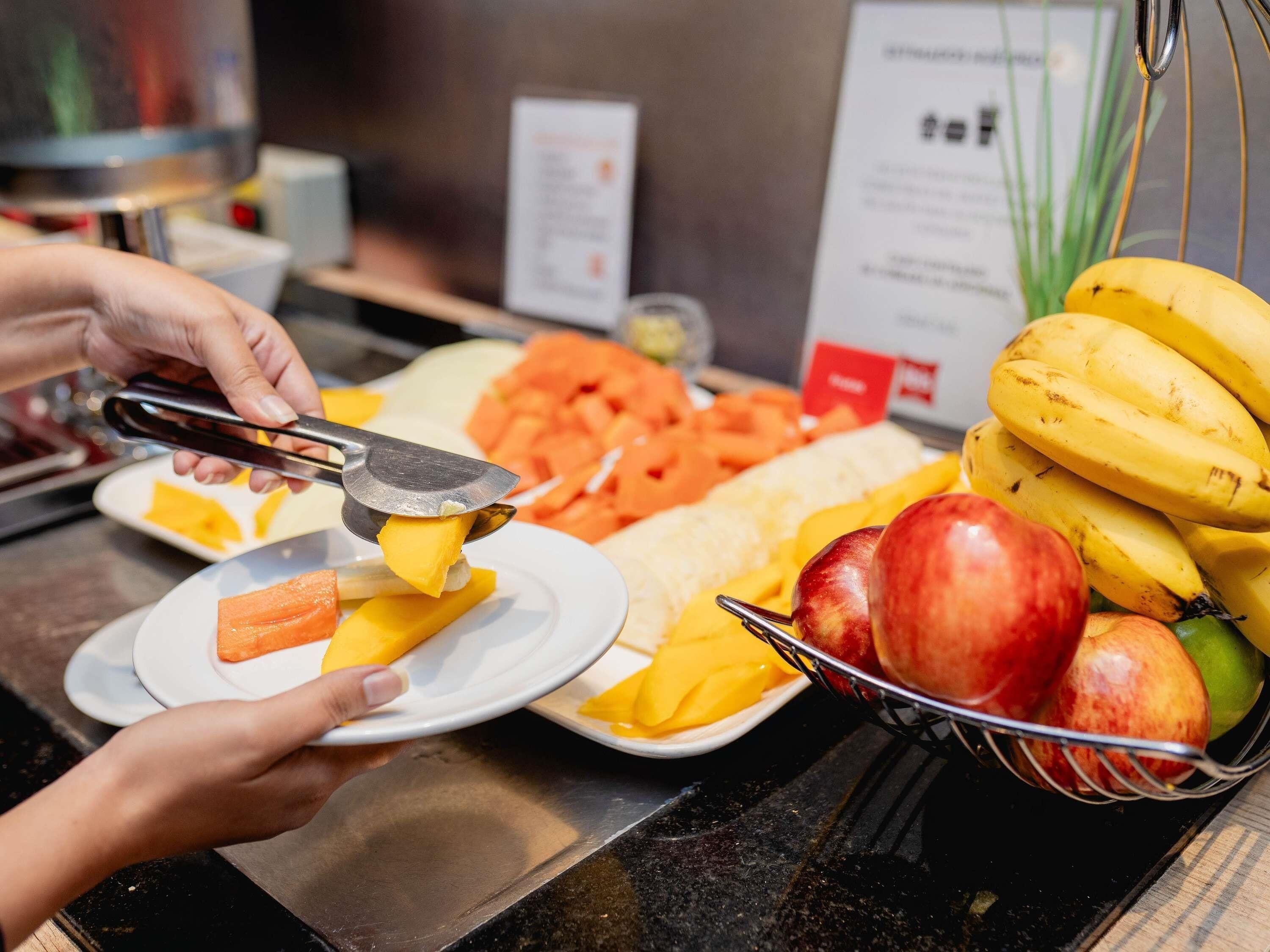 Mostrador de buffet con diversas frutas y verduras, incluyendo plátanos, manzanas y zanahorias.