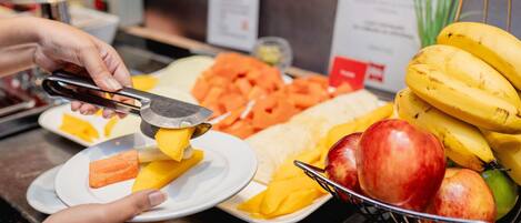 Mostrador de buffet con diversas frutas y verduras, incluyendo plátanos, manzanas y zanahorias.