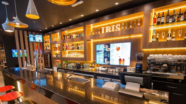Un espace bar comprenant un comptoir, des tabourets, un présentoir pour les menus et une machine à café.