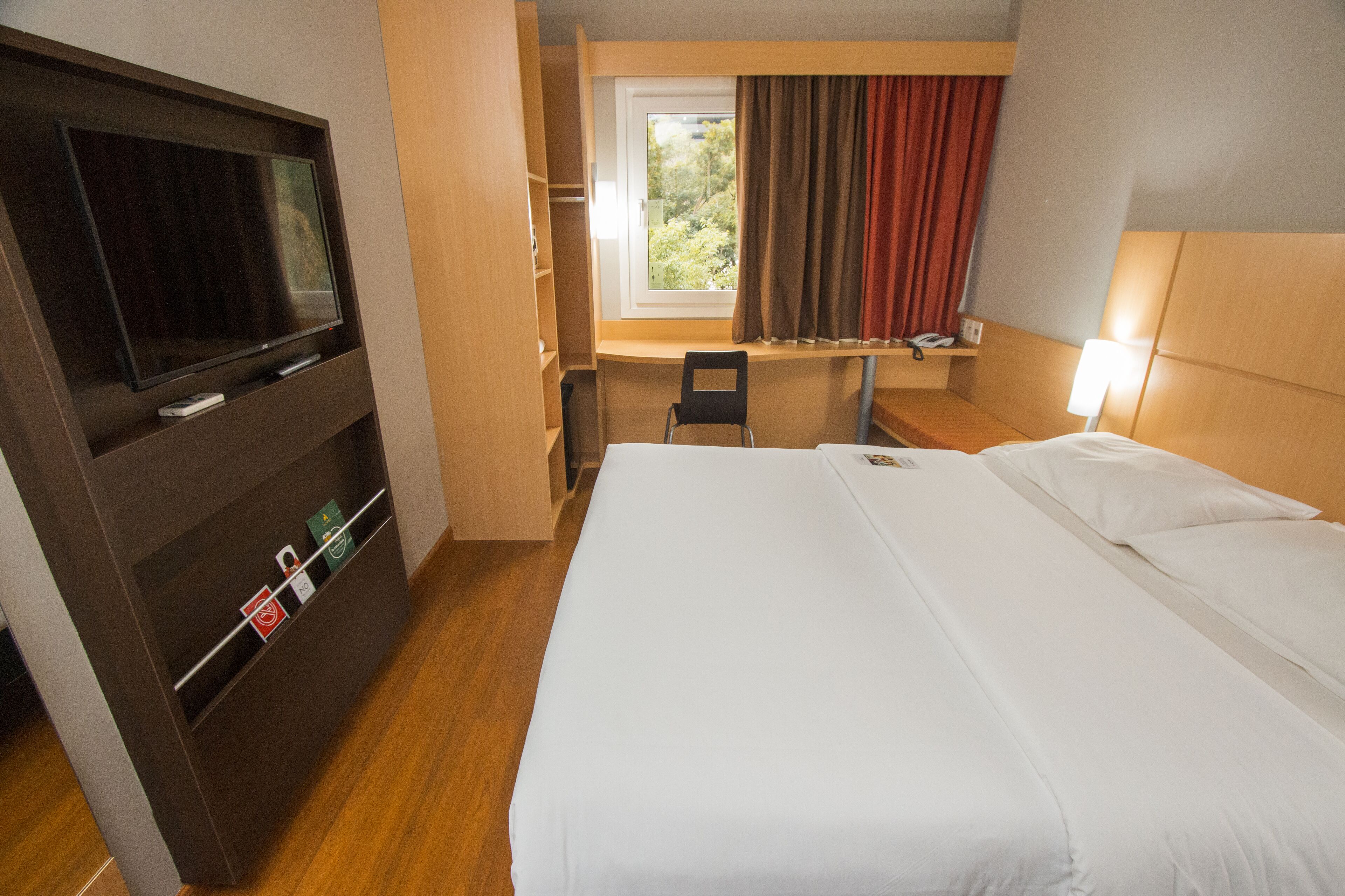A hotel room with a bed, a desk, a TV, and a window with curtains.