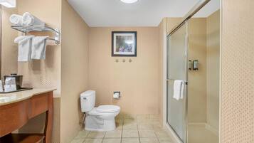 Ein Badezimmer mit Toilette, Waschbecken und Dusche. Handtuchhalter mit Handtüchern, ein gerahmtes Bild an der Wand und ein Toilettenpapierhalter sind vorhanden.