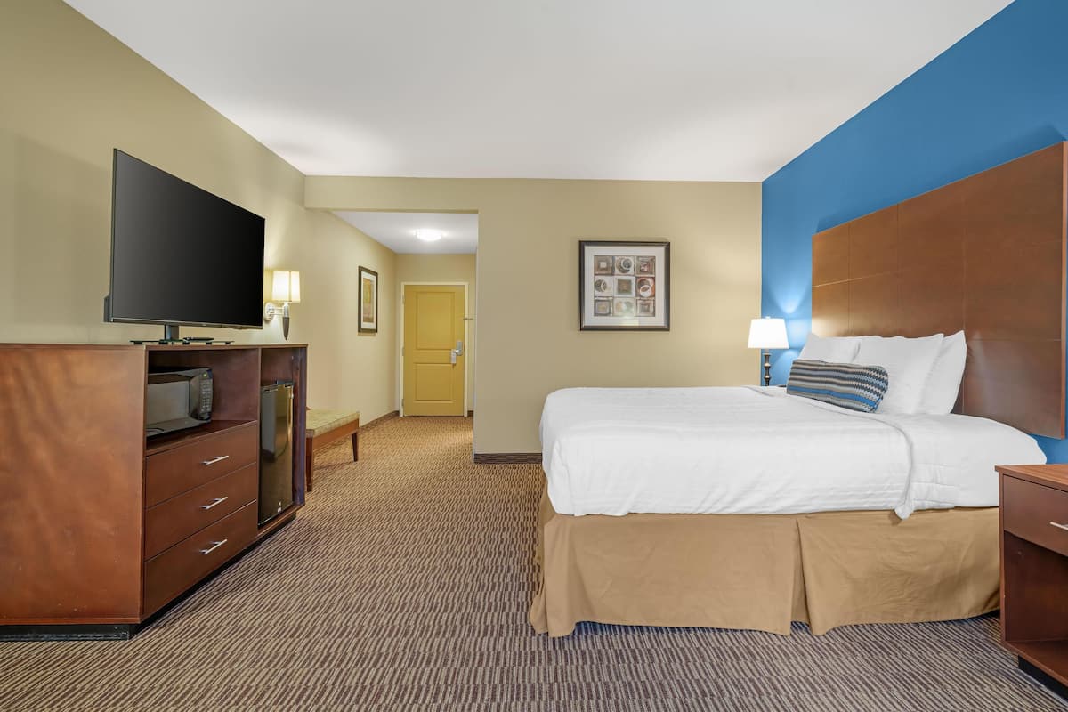 A hotel room with a bed, a TV, a desk, and a door leading to a hallway.