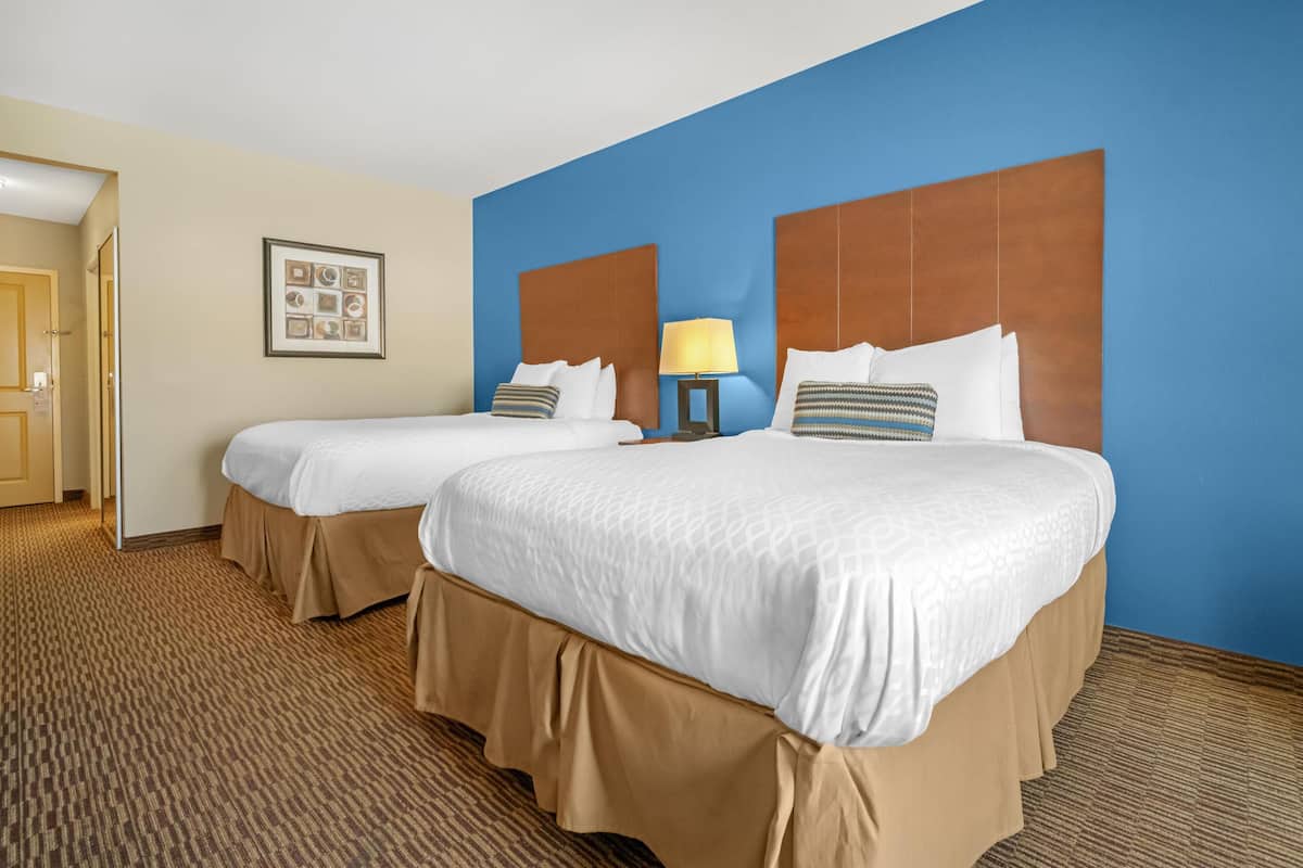 A hotel room with two beds, a blue accent wall, a framed picture, and a carpeted floor.