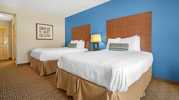 A hotel room with two beds, a blue accent wall, a framed picture, and a carpeted floor.