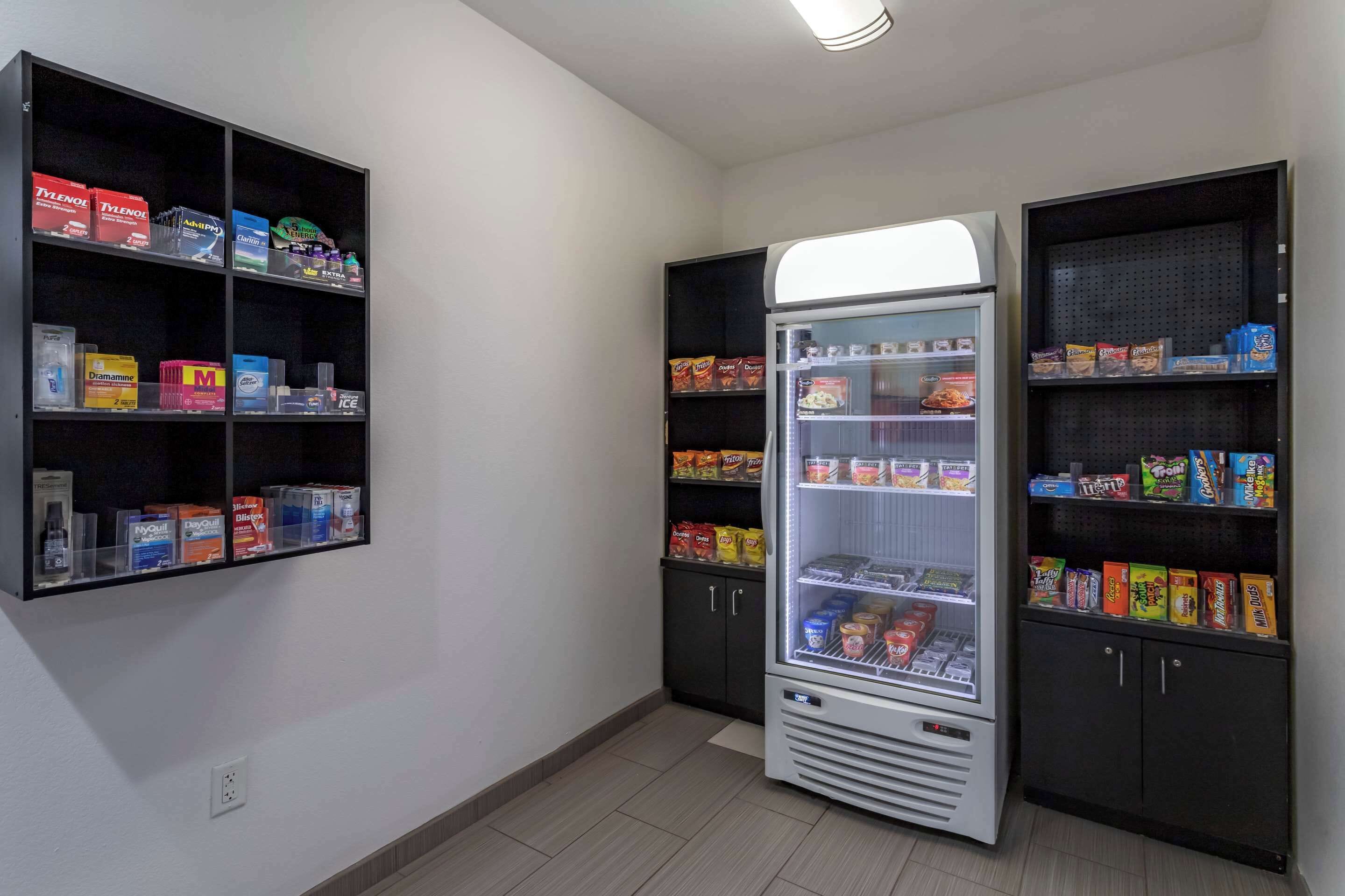 Una habitación pequeña con un refrigerador lleno de aperitivos y bebidas, estantes con diversos alimentos y un armario con más productos alimenticios.