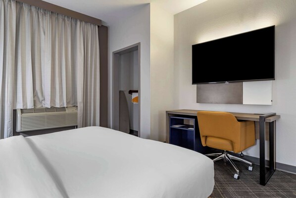 A hotel room with a bed, a desk with a chair, a flat-screen TV, and a wardrobe.