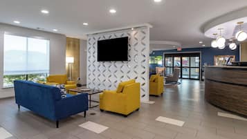 A modern lobby with a blue sofa, yellow armchairs, a flat-screen TV, and a reception desk.