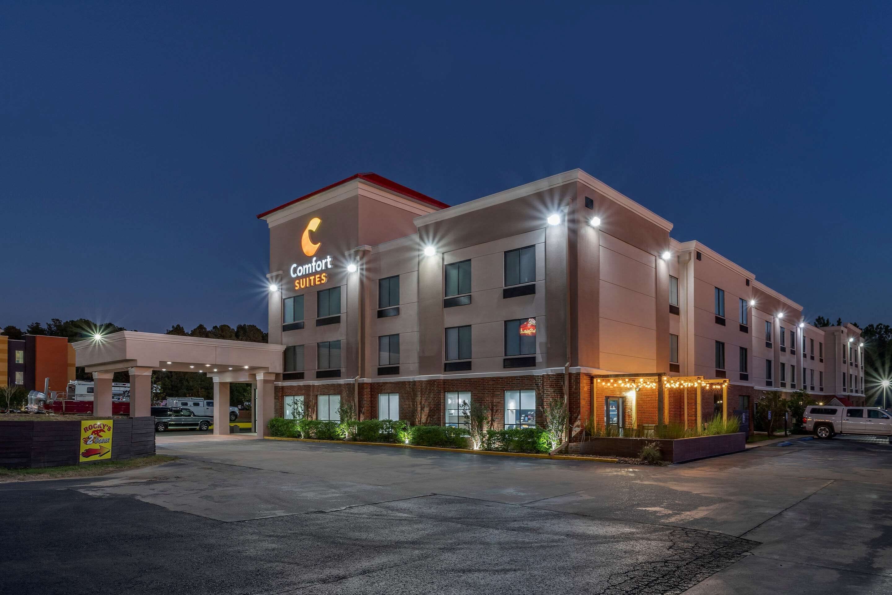 Un hotel con un letrero de 'Comfort Suites', un acceso cubierto y un estacionamiento.