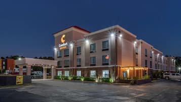 Un hotel con un letrero de 'Comfort Suites', un acceso cubierto y un estacionamiento.