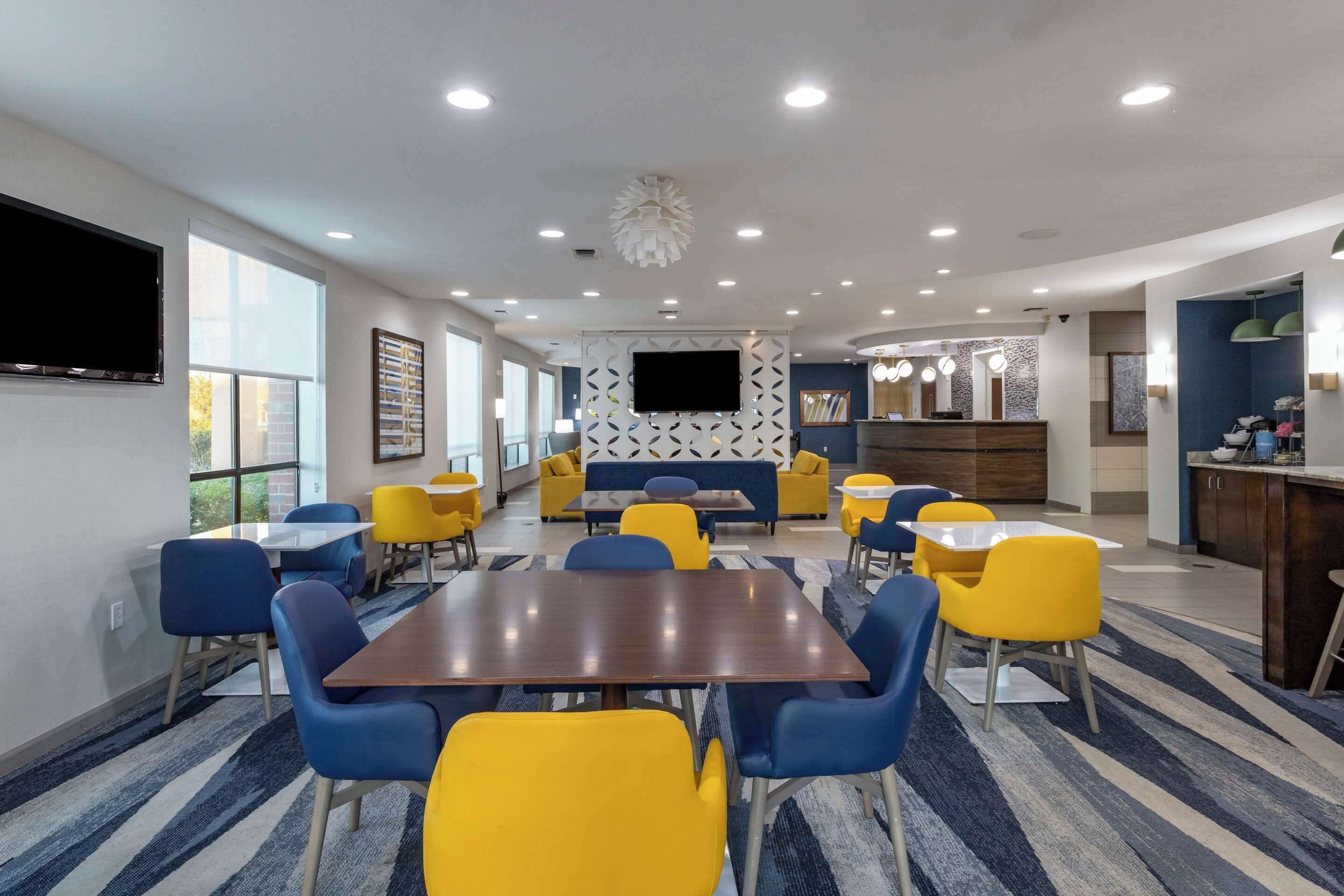 Un hall d’hôtel moderne doté d’un espace salon central, d’un téléviseur à écran plat et d’un coin cuisine.