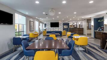 Un hall d’hôtel moderne doté d’un espace salon central, d’un téléviseur à écran plat et d’un coin cuisine.
