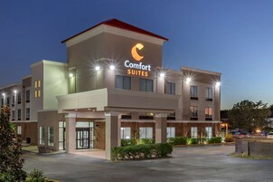 Un hotel moderno con un llamativo letrero de 'Comfort Suites', que presenta un diseño limpio y contemporáneo con techo plano y ventanas amplias.
