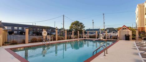 A swimming pool with a fenced area, a small building labeled 'POOL RULES', and a clear sky.