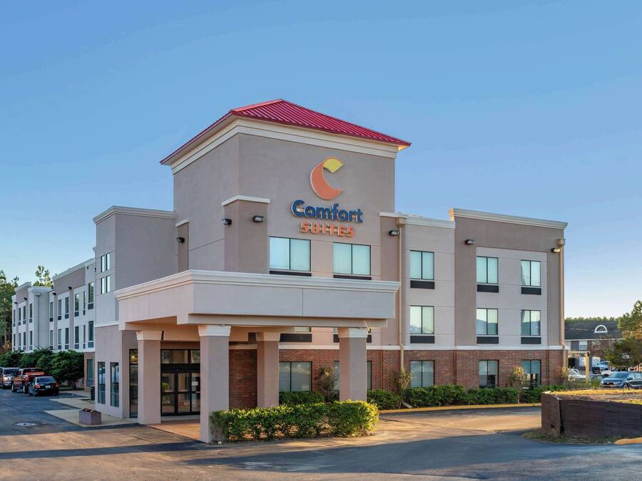 Un hotel Comfort Suites con un diseño moderno, que presenta un logotipo destacado en la fachada, varias ventanas y un estacionamiento.