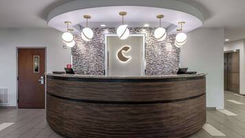A reception area with a circular wooden desk, a modern light fixture, and a brick-patterned wall.