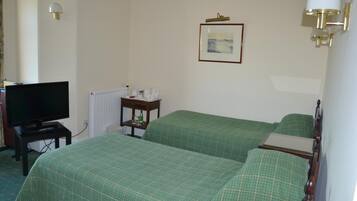 Ein Hotelzimmer mit zwei Betten, einem Fernseher, einem Nachttisch mit Lampe und einem gerahmten Bild an der Wand.