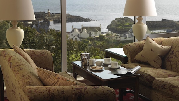 A room with two armchairs facing a large window overlooking a coastal town. - Fernhill Hotel (Stranraer)