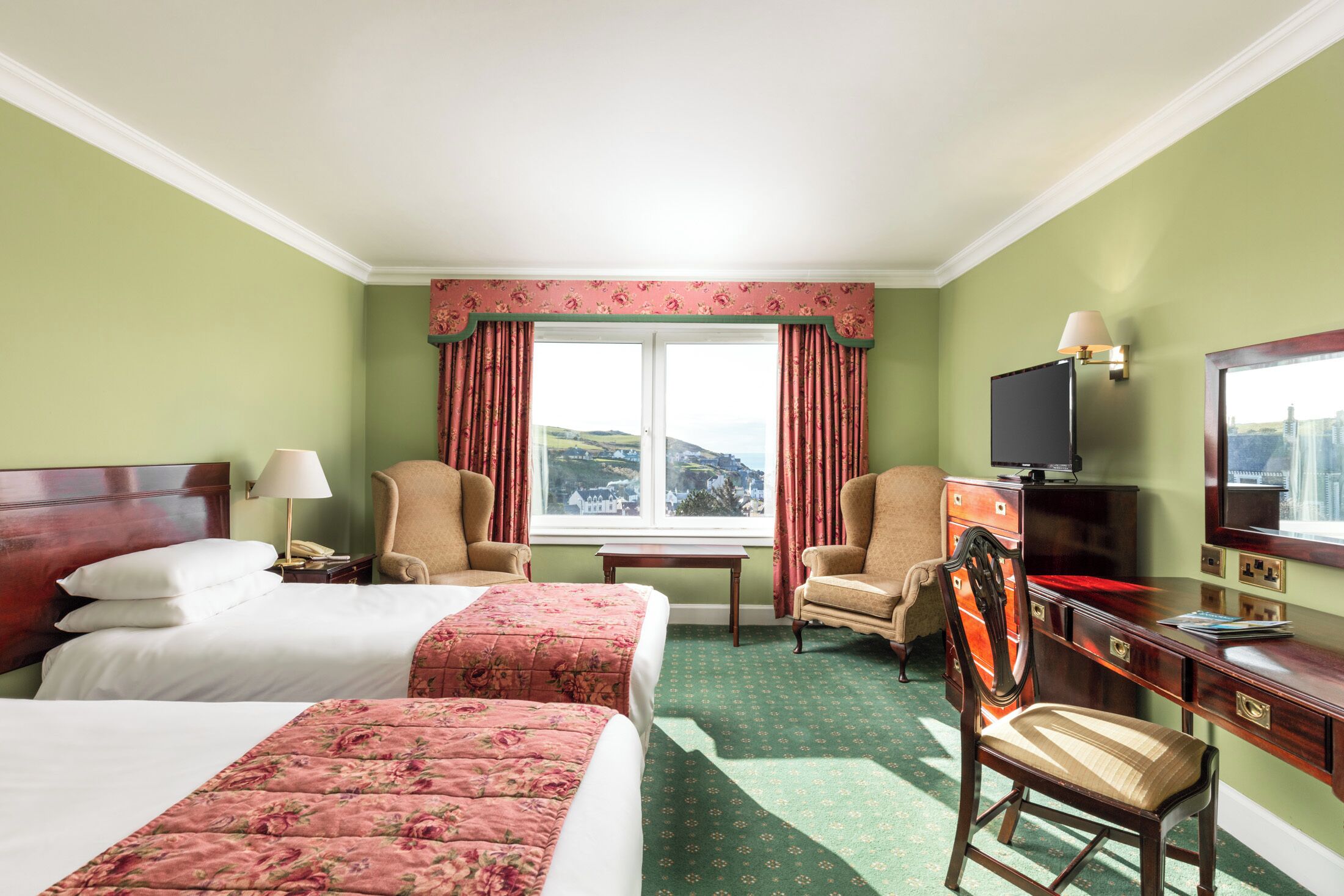 A hotel room with two beds, a desk, a chair, a television, and a window with curtains.
