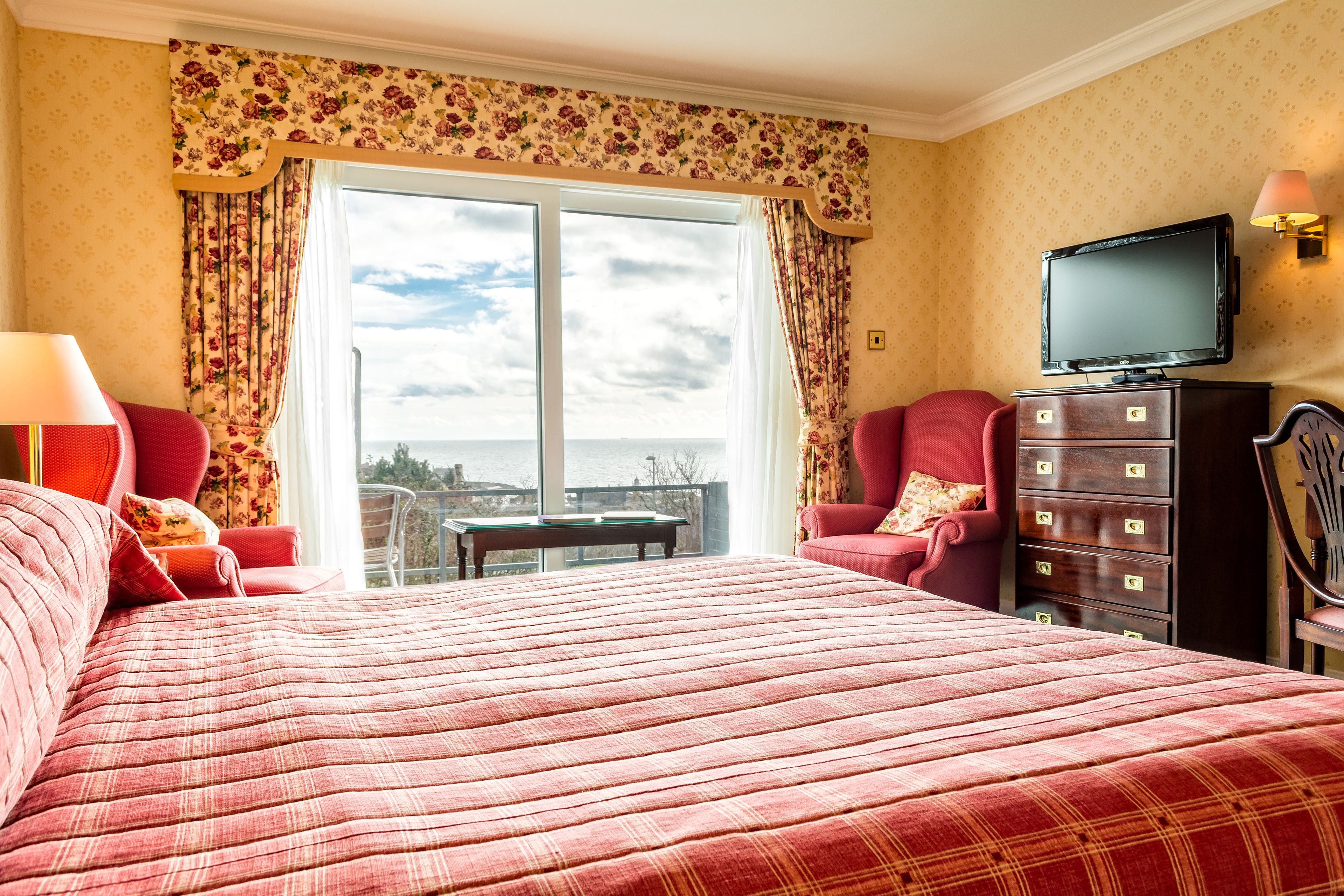 A hotel room with a large bed, a television, a dresser, and a view of the city through the window.