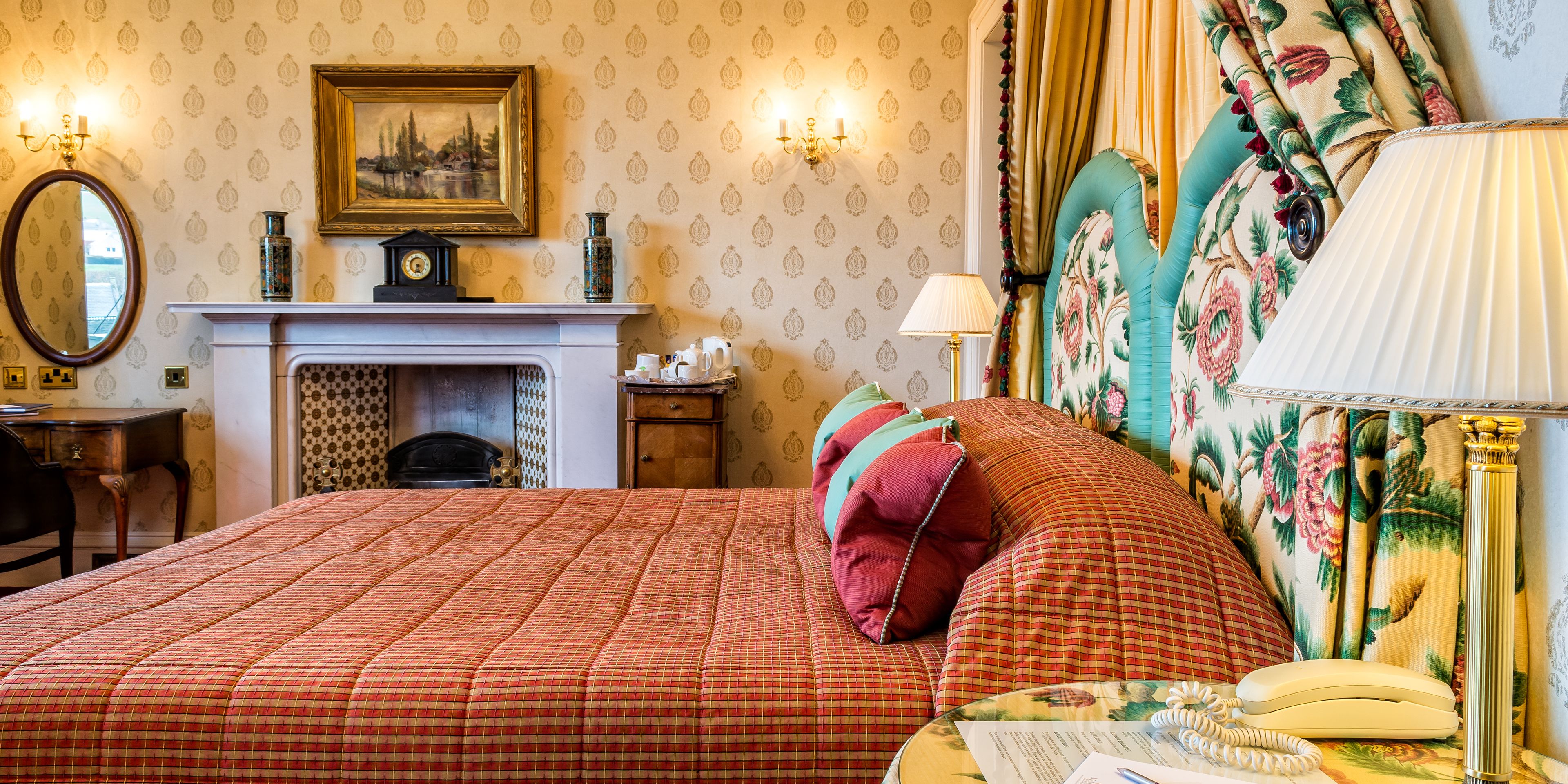 A well-appointed bedroom with a large bed, a fireplace, a desk, and a telephone.